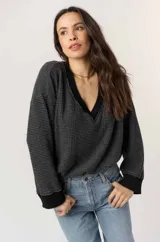 Pullover de tejido tipo waffle, color gris oscuro, con escote en V ribeteado en negro, mangas largas y puños negros contrastantes.