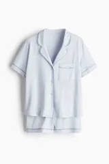Conjunto de pijama corto celeste con ribetes en azul. Incluye camisa de manga corta con cuello abierto, botones y bolsillo en el pecho, y short con cintura elástica.