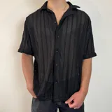 Camisa negra de crochet con cuello camisero, manga corta y cierre frontal con botones.