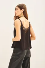 Top tipo musculosa confeccionado en modal satén, color negro, con terminación de calado en el escote delantero y en la espalda, acompañado de bordados a tono.