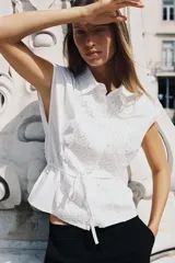 Camisa blanca de popelín con cuello solapa, manga sisa y detalle de guipur floral en el frente. Incluye un cinturón fino del mismo tejido que se ata en la cintura.