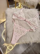 Conjunto de lencería de encaje floral en tonos rosa y crema, compuesto por un corpiño triangular sin aro con breteles finos regulables y una tanga regulable.