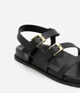 Sandalias negras con tiras de cuero sintético, suela plana y hebillas doradas.
