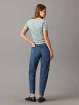Pantalón de jean azul de corte mom, tiro alto, pierna recta y tobillo ajustado. Confeccionado con denim comfort stretch de peso medio, con un 20% de algodón reciclado. Cuenta con bragueta con cremallera, diseño de cinco bolsillos, herrajes de Calvin Klein e insignia de Piel.