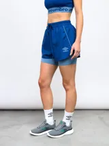 Short deportivo doble capa para mujer, color azul rey. La capa exterior es de tejido texturizado con cordón ajustable en la cintura y ribete blanco en el borde, y la capa interior es una calza corta de color azul claro.