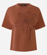 Remera de manga corta color marrón, con cuello redondo y corte recto. Presenta un bordado grande en relieve de una flor en el centro del pecho.