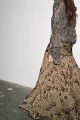 Falda midi de tiro alto con estampado paisley en tonos marrones y dorados. Presenta cintura con drapeado lateral y bajo asimétrico evasé. Cierre con cremallera oculta en la costura.