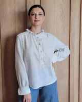 Camisa a rayas verticales color beige y blanco, de corte holgado, con cuello con volados, cierre parcial con botones y mangas largas con puños abotonados.