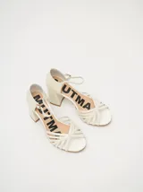 Sandalias negras de charol con tiras cruzadas en el empeine, pulsera con hebilla al tobillo y tacón cuadrado.