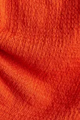 Top naranja sin mangas, de punto texturizado con escote bote y cordones ajustables en un lateral y en un hombro para crear un efecto drapeado.