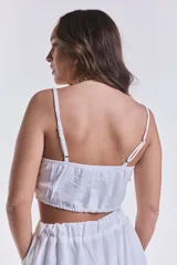 Crop top blanco con breteles finos regulables y elástico en la espalda. Presenta un nudo en el centro del busto.
