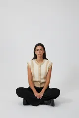 Chaleco sin mangas de acrílico, color beige y crema, con volados en los laterales y cierre frontal con botones.