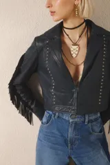 Campera corta de cuero color negro, con flecos en espalda y mangas, tachas metálicas y símil piedra cristal. Cierra con broches en el frente, tiene forrería y bolsillo interno.