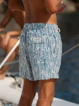 Short de baño azul con estampado de líneas verticales en tonos de azul y blanco. Tiene elástico en la cintura, cordón ajustable, tres bolsillos y mesh interior hipoalergénico.