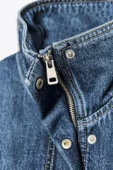 Chaqueta corta de denim azul con cuello alto, manga larga con hombros caídos, bolsillos laterales, bajo con elástico y cierre frontal con cremallera y botones ocultos.
