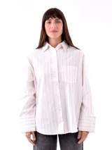 Camisa blanca con rayas verticales negras, de corte holgado, manga larga con puños abotonados y bolsillo en el pecho.