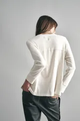 Remera negra de algodón con calce relajado, cuello redondo y mangas largas. Presenta una abertura frontal con arandelas metálicas y cordón.