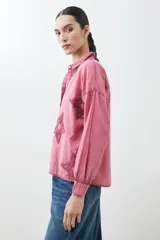Camisa fucsia de manga larga con cuello camisero y cierre frontal con botones. Presenta apliques de estrellas bordadas en el frente y en el cuello.