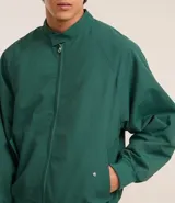 Campera bomber verde oscuro de poliéster con cuello alto con velcro, cierre por cremallera, bolsillos con solapa, manga larga ajustada y bajo ajustado.