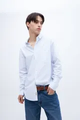Camisa celeste con rayas verticales blancas, de corte regular, con cuello solapa clásico, bolsillo en el pecho y botones personalizados.