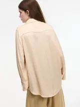 Camisa color durazno de corte amplio y fluido, con botones frontales y mangas largas.