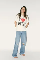 Remera color crudo de corte holgado con mangas cortas y cuello redondo. Estampado frontal con el texto "I ❤️ NY" en color negro y rojo.