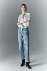 Pantalón de jean de tiro alto, denim azul rígido con lavado localizado y apliques de brillos. Pierna recta y ruedo desflecado.