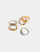 Set de cinco anillos de metal con diferentes diseños: uno dorado con textura de líneas horizontales, uno plateado con textura trenzada, uno dorado con forma de croissant, uno dorado con textura de líneas horizontales y uno plateado con diseño doble.