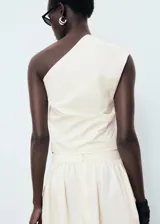 Top de algodón color crema, con cuello asimétrico, detalle de bordado floral en el hombro y frunces laterales. Cierre lateral con cremallera.