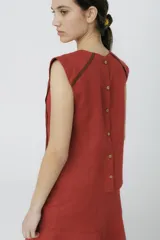 Blusa color ladrillo con cuello redondo y sin mangas, con ribete marrón en los bordes.