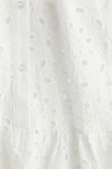 Vestido corto blanco de algodón con broderie, cuello alto con volados, mangas cortas con volados, botonadura frontal y falda con volados.