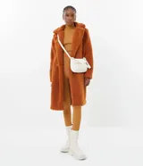 Campera larga de sherpa color marrón, con cuello solapa, cierre con botones y bolsillos laterales. Forro de poliéster.