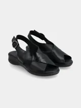 Sandalia negra con tiras cruzadas en el empeine, una de cuero liso y otra con textura. Tiene tira trasera con hebilla y suela baja.