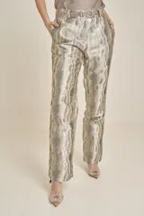 Pantalón de vestir con estampado abstracto en tonos plateados y dorados, con cinturón plateado.