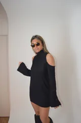 Vestido negro de punto, con cuello alto y mangas largas con cortes en los hombros.