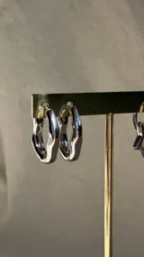Aros tipo argolla plateados, con forma orgánica y fluida, que simulan un metal maleable. Tienen un pequeño detalle dorado en el cierre.
