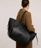 Bolso shopper grande de cuero sintético negro con asas medianas y cierre de cremallera. Incluye un dije colgante en forma de corazón y una pequeña cartera extra.