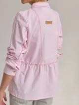 Camisa celeste de algodón con cuello clásico, cierre frontal con botones y mangas largas. Presenta volados en el frente y corte evasé.