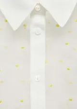 Camisa blanca semitransparente con bordado de flores, cuello camisero, manga corta y cierre frontal con botones.