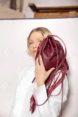 Cartera tipo saco color bordó, confeccionada en cuero, con cierre de cordón ajustable y flecos largos en la parte inferior. Incluye correa de hombro fina.
