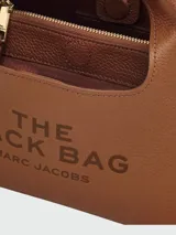 Bolso blanco tipo hobo, modelo The Mini Sac Bag de Marc Jacobs, con asas cortas y texto estampado en el frente.