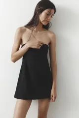 Vestido corto negro sin mangas, con escote palabra de honor y pespuntes marcados. Cierre trasero con cremallera oculta.