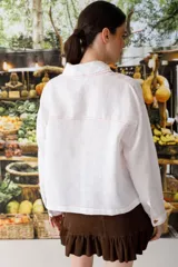 Blusa blanca de lino con cuello polo, manga larga y botones dorados. Presenta costuras a contratono en color naranja.