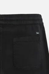Bermuda color verde militar de corte relajado, confeccionada en tejido de algodón. Tiene cintura elástica ajustable con cordón interior, bolsillos frontales y bolsillo trasero de parche.