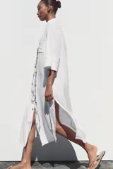 Vestido camisero largo color verde claro, confeccionado en lino. Tiene cuello solapa, escote en V, manga tres cuartos con trabilla y botón, bolsillos delanteros de plastrón, aberturas laterales en el ruedo y cierre frontal con botones.