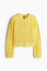 Cárdigan amarillo de tejido de punto calado, con cuello redondo, manga larga y cierre frontal con botones. Tiene terminaciones acanaladas en cuello, puños y ruedo.