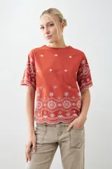 Remera color ladrillo con bordado de flores blancas en el ruedo y las mangas.