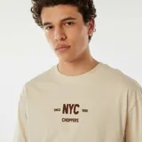 Remera color beige de corte recto y manga corta, con estampa frontal de la inscripción "NYC" en color marrón.
