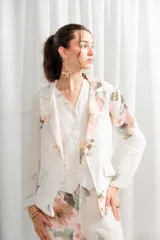 Blazer de lino blanco con estampado floral en tonos rosa y verde, corte holgado, cuello solapa y bolsillos laterales.