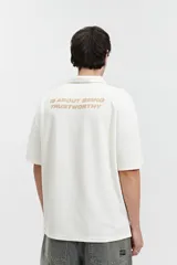 Remera polo color beige con textura acanalada, corte oversize, cuello clásico con botones y logo estampado en el pecho.